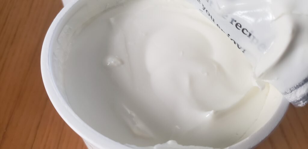 Open tub of thick plain skyr, lid peeled back, smooth and cold.